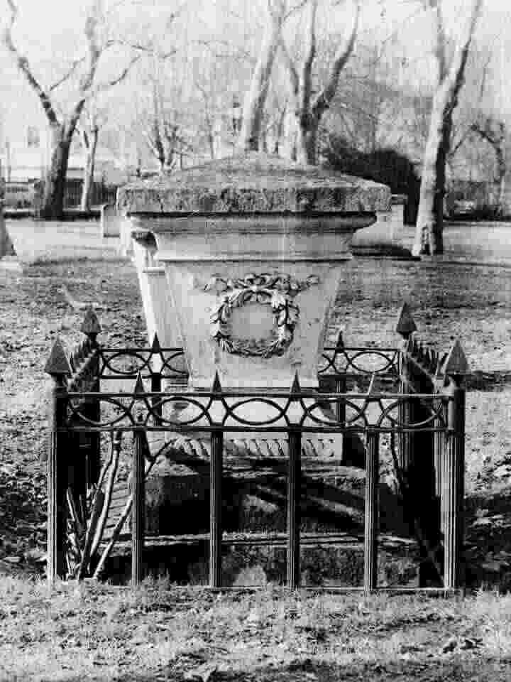 A black and white photo of an ornate grave, surrounded by low fencing.