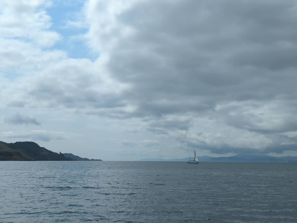 A view out into the Sound of Jura. A yacht is passing left to right, and some headland is sticking out on the left. Some large suspicious rainclouds are gathering.