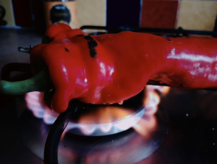 A red sweet pointed pepper roasting on a gas hob.